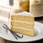 Slice of fluffy homemade vanilla cake with creamy white frosting and sprinkles on a plate